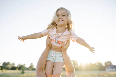 Mother lifting happy cute girl with arms outstretched in field on sunny day - SSYF00148