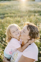 Mother kissing happy daughter in summer field - SSYF00149