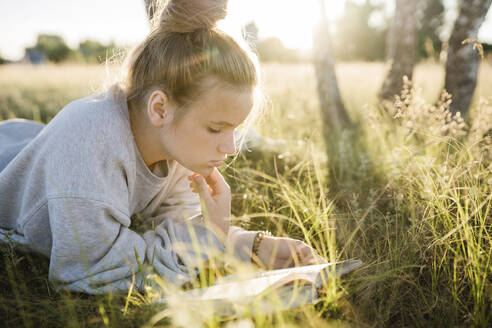 Girl lying on grass and reading book on sunny day - SSYF00152