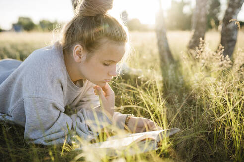 Mädchen liegt im Gras und liest ein Buch an einem sonnigen Tag - SSYF00152