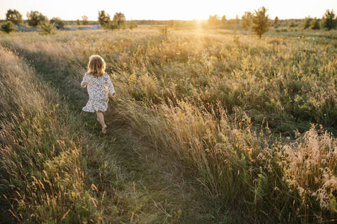 Unbekümmertes Mädchen, das an einem Sommerabend im Feld läuft - SSYF00155
