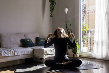 Frau macht Yoga auf Matte sitzend im Wohnzimmer zu Hause - RFTF00383