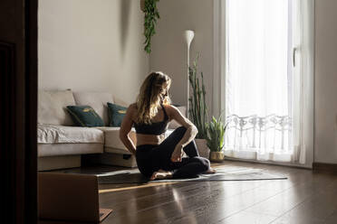 Woman practicing yoga on mat in living room at home - RFTF00384