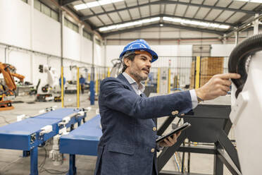 Ingenieur mit Schutzhelm bei der Prüfung von Maschinenteilen in einer Fabrik - JCCMF09664