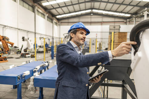 Ingenieur mit Schutzhelm bei der Prüfung von Maschinenteilen in einer Fabrik - JCCMF09664