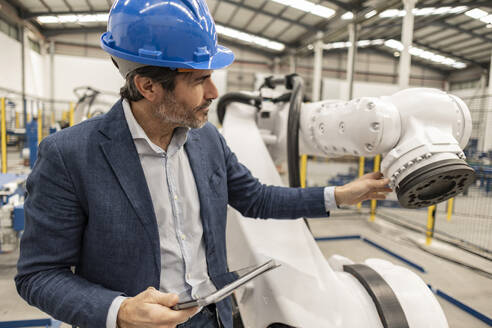 Engineer with tablet PC examining robotics part in factory - JCCMF09665