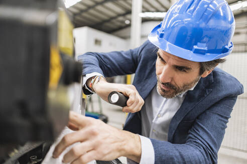 Ingenieur mit Brenner bei der Analyse eines Maschinenteils in einer Fabrik - JCCMF09674