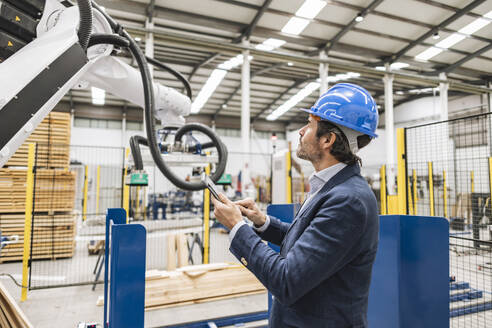 Engineer examining robotic arm using tablet computer in factory - JCCMF09677