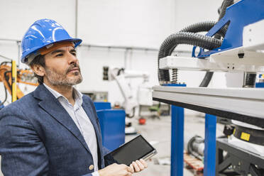 Ingenieur mit Schutzhelm bei der Prüfung von Maschinenteilen in einer Fabrik - JCCMF09679