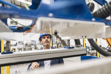 Nachdenklicher Ingenieur bei der Betrachtung von Maschinenteilen in einer Fabrik - JCCMF09680