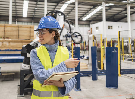 Junger Ingenieur mit Notizblock und Stift, der in einer Fabrik zeigt - JCCMF09688