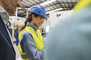 Glücklicher Ingenieur mit Schutzhelm und Kollegen in einer Fabrik - JCCMF09693