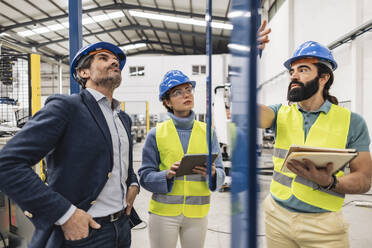 Engineer with note pad explaining colleagues in factory - JCCMF09699