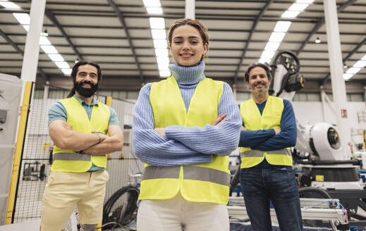 Confident engineers standing with arms crossed in robotics factory - JCCMF09752