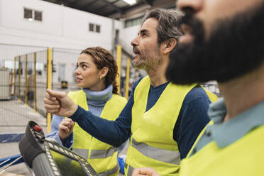 Engineer holding control panel working with colleagues in factory - JCCMF09762