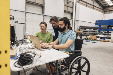 Engineer sitting in wheelchair working with colleagues in factory - JCCMF09786