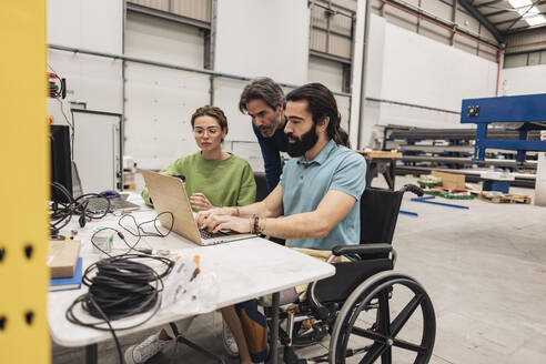 Ingenieur im Rollstuhl sitzend bei der Arbeit mit Kollegen in der Fabrik - JCCMF09786