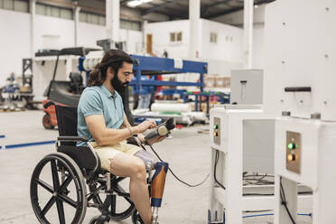 Ingenieur im Rollstuhl sitzend bei der Steuerung einer Maschine in der Industrie - JCCMF09795