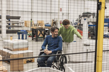 Mature engineer sitting in wheelchair discussing with colleague in factory - JCCMF09796