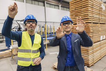 Älterer Ingenieur mit einem Kollegen, der eine intelligente Brille trägt, gestikuliert in einer Fabrik - JCCMF09809
