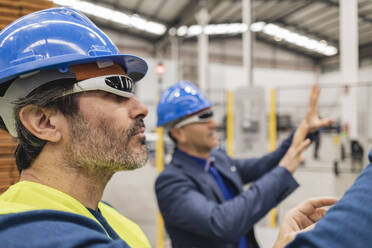 Älterer Ingenieur mit intelligenter Brille, der neben einem Kollegen in einer Fabrik steht - JCCMF09811