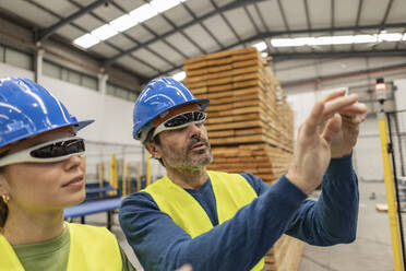 Mature engineers wearing smart glasses gesturing in factory - JCCMF09823