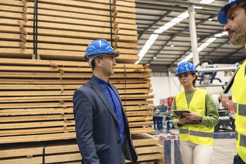 Älterer Ingenieur diskutiert mit Kollegen an einem Stapel von Brettern in einer Fabrik - JCCMF09832