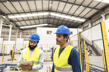 Engineer with colleague writing notes in robotics factory - JCCMF09834