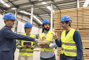 Mature engineer explaining colleagues over note pad in factory - JCCMF09835