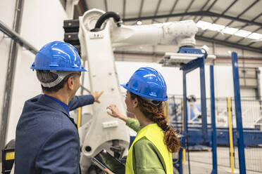 Engineers wearing hardhat having discussion in front of robotic arm at factory - JCCMF09846