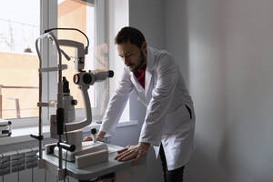 Doctor examining eye scanner machine at clinic - SANF00075