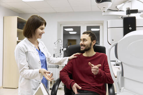 Lächelnder Augenarzt im Gespräch mit einem Patienten in der Klinik - SANF00082