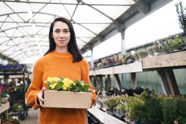 Junge Frau mit einer Kiste mit gelben blühenden Pflanzen in einem Gartencenter - AMWF01216