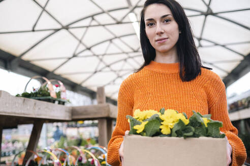 Frau mit Kiste mit gelben blühenden Pflanzen in einem Gartencenter stehend - AMWF01217