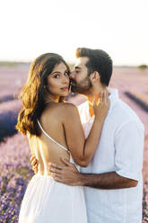 Mann küsst Frau auf die Wange stehend im Lavendelfeld - JJF00375