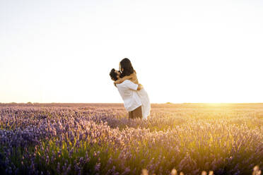 Mann trägt Frau in Lavendelfeld bei Sonnenuntergang - JJF00384
