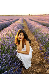 Junge Frau hockt bei Lavendelpflanzen im Feld - JJF00397