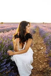 Glückliche junge Frau hockt in einem Lavendelfeld - JJF00399