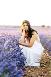 Frau hockt bei Sonnenuntergang bei Lavendelpflanzen im Feld - JJF00400