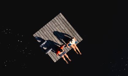 Mann und Frau sitzen auf dem Rand einer Badeplattform auf einem See im Sommer. - CAVF96671
