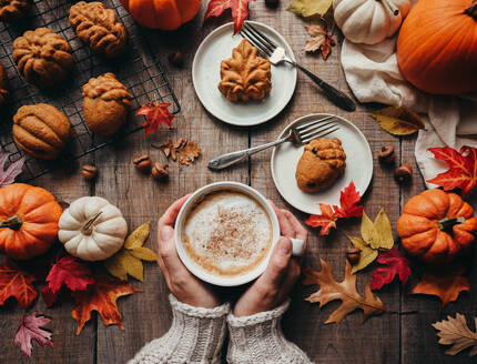 Draufsicht auf herbstlich geformte Kürbisgewürzkuchen und Hände, die Milchkaffee halten. - CAVF96673