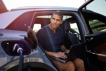 Nachdenklicher Mann mit Laptop im Auto sitzend - CAVF96711