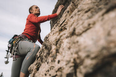 A woman in a red shirt rock climbing on a sunny day. - CAVF96736