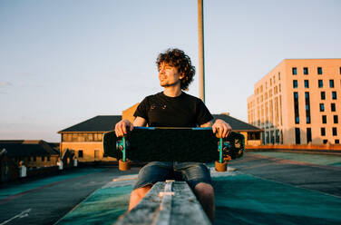 Porträt eines Mannes in der Stadt mit seinem Skateboard zur goldenen Stunde - CAVF96748