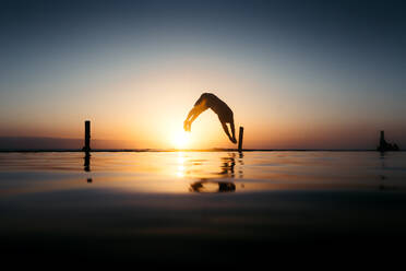 Silhouette eines jungen Mannes, der bei Sonnenuntergang in den Pool springt - CAVF96776