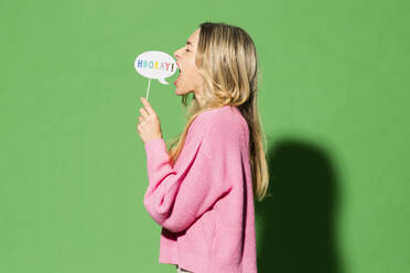 Frau hält Sprechblase und schreit vor grünem Hintergrund - MIKF00150