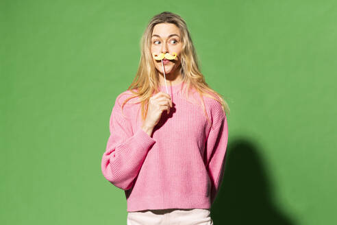 Frau imitiert Schnurrbart vor grünem Hintergrund - MIKF00155