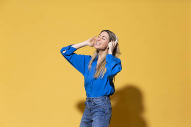 Carefree woman enjoying listening to music against yellow background - MIKF00176