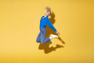 Carefree woman jumping in joy against yellow background - MIKF00185