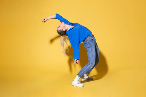 Woman with hand raised dancing against yellow background - MIKF00186